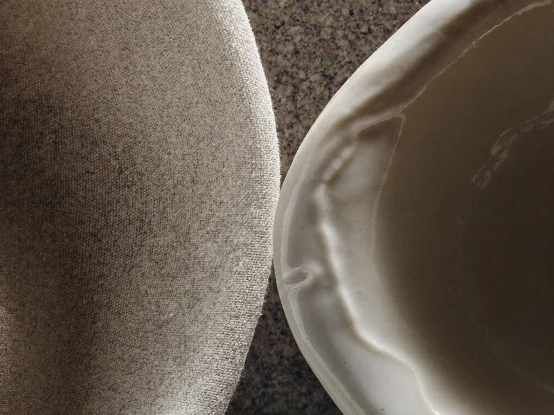 Detaliu macro: țesătură de in crud lângă marginea unei glazuri ceramice